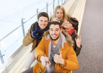 people, friendship, technology and leisure concept - happy friends taking selfie with camera or smartphone and selfie stick on skating rink