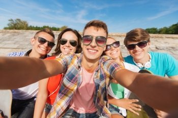 friendship, leisure, summer, technology and people concept - group of smiling friends with skateboard making selfie outdoors