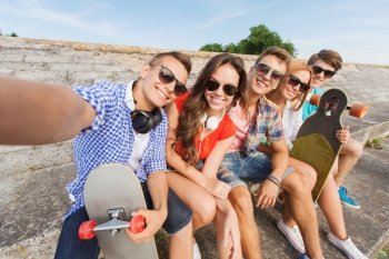 friendship, leisure, summer, technology and people concept - group of smiling friends with skateboard making selfie outdoors