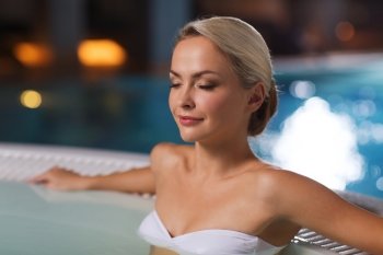 people, beauty, spa, healthy lifestyle and relaxation concept - beautiful young woman wearing bikini swimsuit sitting in jacuzzi at poolside