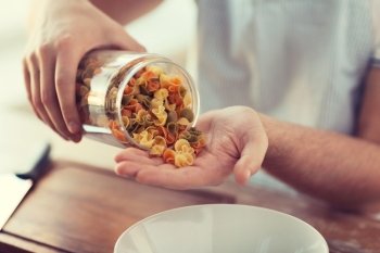 cooking and home concept - close up of male emptying jar with colorful pasta