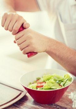 cooking and home concept - close up of male hands flavouring salad in a bowl