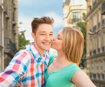 travel, tourism, summer vacation, technology and love concept - happy couple taking selfie with smartphone or camera and kissing over city street background