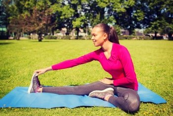 fitness, sport, training, park and lifestyle concept - smiling african american woman stretching leg on mat outdoors