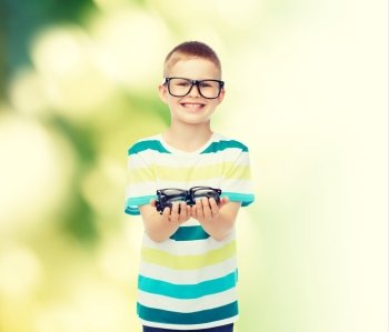 vision, health, ecology and people concept - smiling little boy in eyeglasses holding spectacles over green background