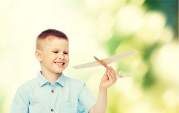 dreams, future, hobby, ecology and childhood concept - smiling little boy holding wooden airplane model in his hand over green background