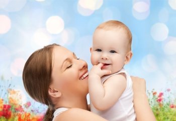 people, family, motherhood and children concept - happy mother hugging adorable baby with finger in his mouth over blue lights and poppy field background