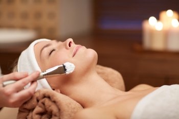 people, beauty, spa, cosmetology and skincare concept - close up of beautiful young woman lying with closed eyes and cosmetologist applying facial mask by brush in spa