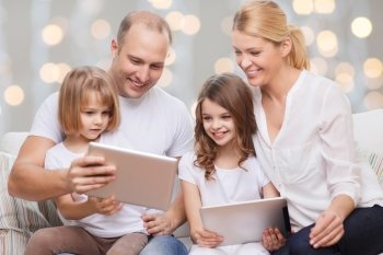 family, children, technology and people concept - smiling parents and two little girls with tablet pc computers over holidays lights background