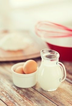 cooking and food concept - close up of jugful of milk, eggs in a bowl and flour