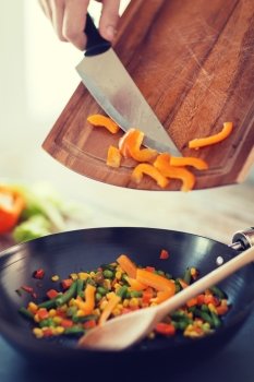 cooking, food and home concept - close up of male hand adding peppers to wok