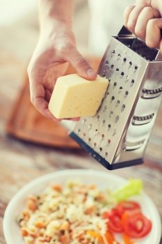 cooking, food and home concept - close up of male hands grating cheese over pasta