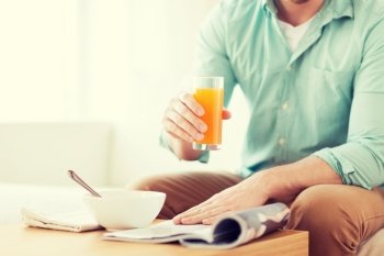 home, news, food, drinks and people concept - close up of man reading magazine and drinking juice sitting on couch at home