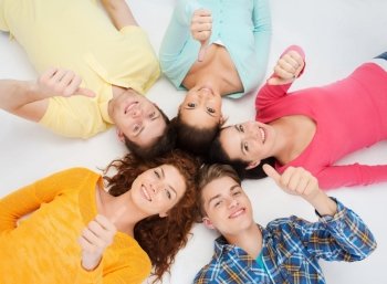 friendship, youth, gesture and people - group of smiling teenagers lying on floor in a circle and showing thumbs up