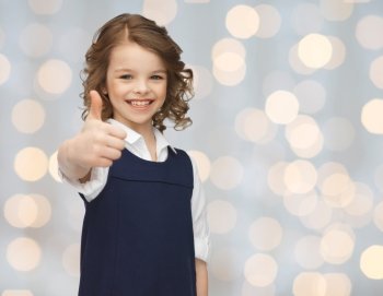 people, gesture, children, summer vacation and happiness concept happy little school girl showing thumbs up over holidays lights background