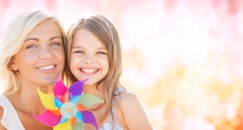 summer holidays, family, children and people concept - happy mother and girl with pinwheel toy over pink lights background