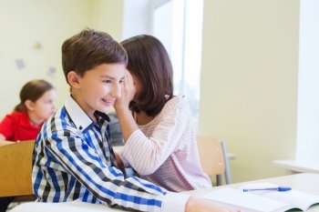 education, elementary school, learning and people concept - smiling schoolgirl whispering secret to classmate ear in classroom