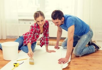 repair, building and home concept - smiling couple smearing wallpaper with glue