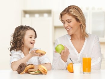 people, healthy lifestyle, family and food concept - happy mother and daughter eating healthy breakfast over home kitchen background