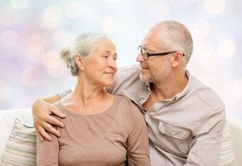 family, relations, love, age and people concept - happy senior couple hugging and looking at each other on sofa over holidays lights background