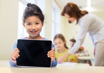 education, elementary school, technology, advertisement and children concept - little student girl showing blank black tablet pc computer screen over classroom and classmates background