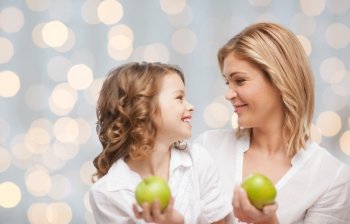 people, family, healthy eating and parenting concept - happy mother and daughter with green apples over lights background