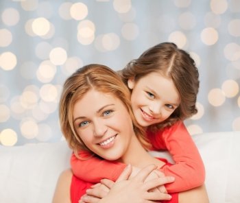 people, happiness, love, family and motherhood concept - happy mother and daughter hugging over holidays lights background
