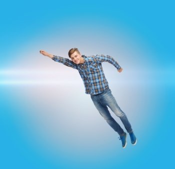 happiness, freedom, movement and people concept - smiling young man flying in air over blue background with laser light