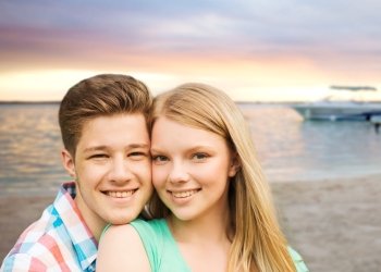 holidays, vacation, love and people concept - smiling teenage couple hugging over sunset beach background