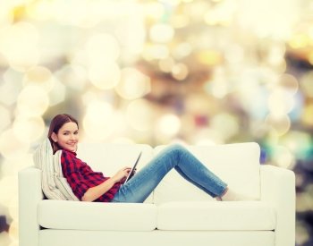 technology and happy people concept - teenage girl sitting on sofa with tablet pc