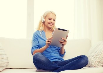 home, music, technology and internet concept - smiling woman sitting on the couch with tablet pc computer and headphones at home
