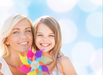 summer holidays, family, children and people concept - happy mother and girl with pinwheel toy over blue lights background