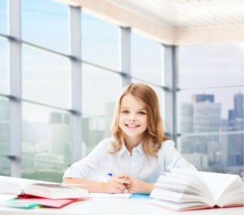 education, people, children and school concept - happy student girl sitting at table with books and writing in notebook over classroom background