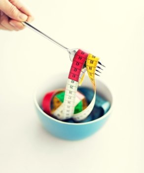 sport and diet concept - woman hand with fork, bowl and measuring tape
