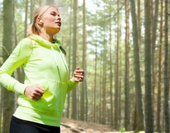 people, sport, fitness and slimming concept - happy woman running or jogging over woods background