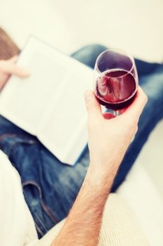 leisure, drinks, education and lifestyle concept - close up of male hand holdind book and glass of red wine