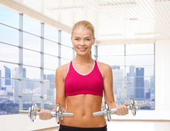 fitness, sport, fitness and people concept - smiling woman with dumbbells flexing biceps over gym or home background
