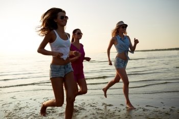 summer vacation, holidays, travel and people concept - group of smiling young women in sunglasses and casual clothes running on beach