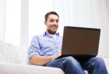 technology, home, people and lifestyle concept - smiling man working with laptop at home
