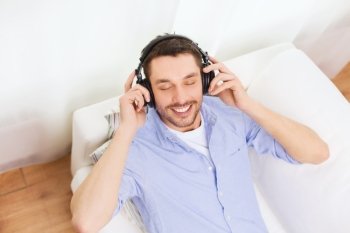 technology, leisure, people and happiness concept - smiling young man with closed eyes in headphones listening to music at home