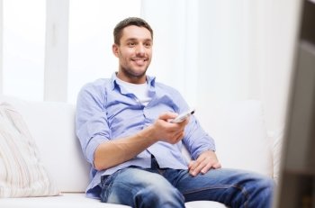 home, technology, people and entertainment concept - smiling man with tv remote control at home