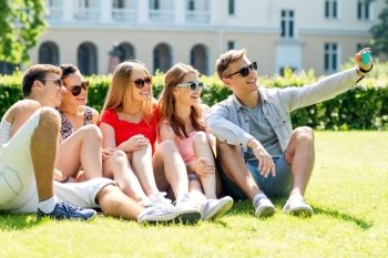 friendship, leisure, summer, technology and people concept - group of smiling friends with smartphone making selfie in park
