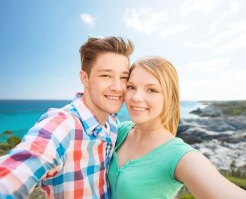 people, love, vacation, technology and summer concept - happy couple taking selfie with smartphone or camera over sea shore background