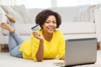 people, internet bank, online shopping, technology and e-money concept - happy african american young woman lying on floor with laptop computer and credit card at home