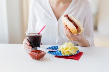 american independence day, celebration, patriotism and holidays concept - close up of woman hands holding hot dog and coca cola in plastic cup with potato chips and ketchup on 4th july at home party
