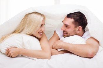 people, family, bedtime and happiness concept - happy couple lying in bed covered with blanket over head and talking at home
