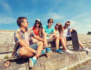 friendship, leisure, summer and people concept - group of smiling friends with skateboards sitting on city street