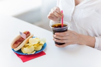 american independence day, celebration, patriotism and holidays concept - close up of woman drinking coca cola from plastic cup with hot dog and potato chips on 4th july at home party