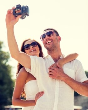 love, wedding, summer, dating and people concept - smiling couple wearing sunglasses making selfie with digital camera in park