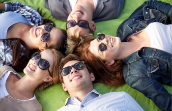 summer holidays, friendship, leisure and teenage concept - group of students or teenagers lying in circle at campus or park
